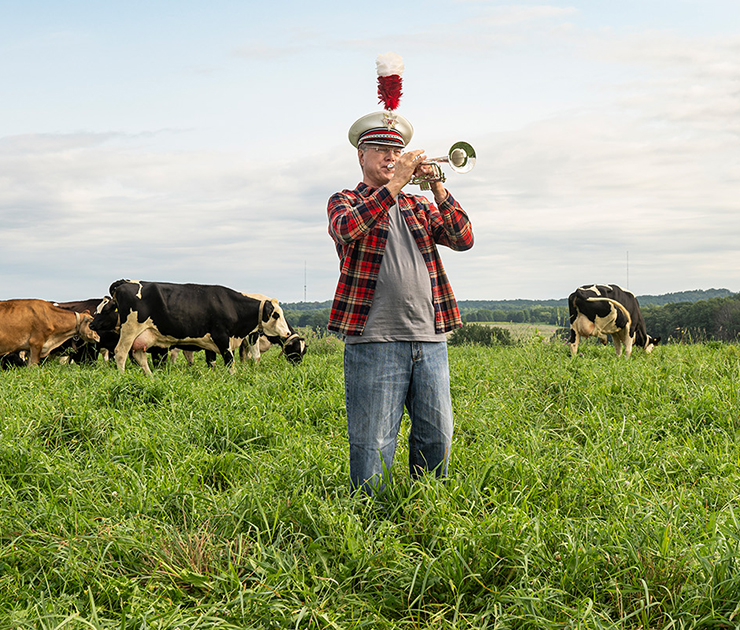UW–Madison marching band alumni playing the trumpet in a field with dairy cows. Image is part of UW’s 30 second Band Together tv commercial